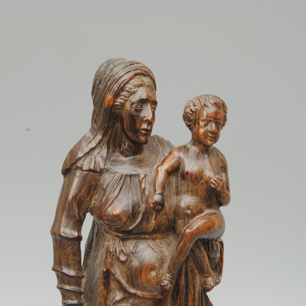 A dark hardwood carving of the Madonna standing in draped robes whilst holding the Christ child. View III