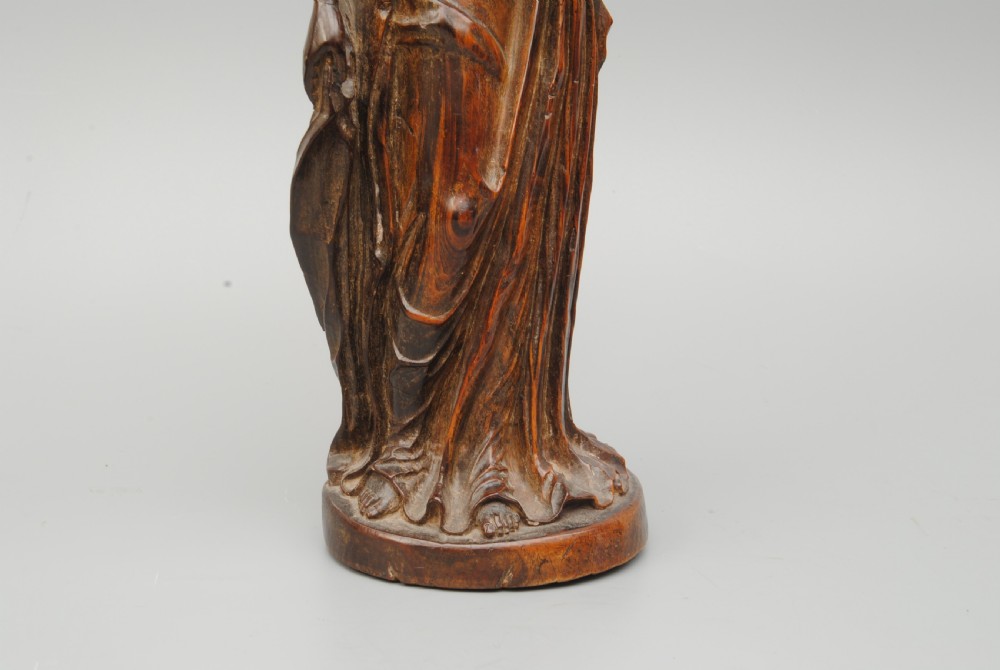 A dark hardwood carving of the Madonna standing in draped robes whilst holding the Christ child. View V