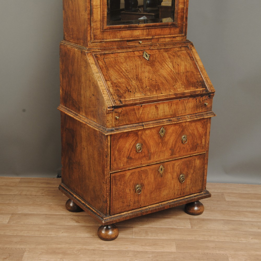 A compact Queen Anne walnut bureau bookcase featuring an arched mirror door upper section above a slant-front desk and two drawers on bun feet. View IV
