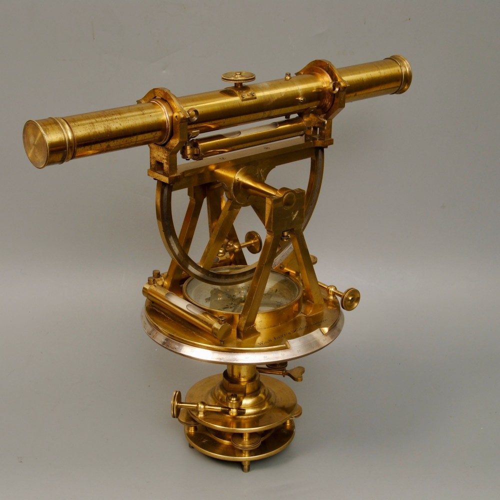 An antique brass radial theodolite featuring an adjustable telescope mounted above a compass dial, spirit level vials, and a graduated horizontal plate.