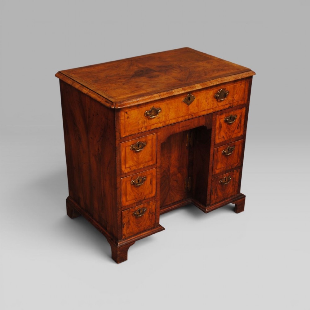 An 18th-century Queen Anne burr walnut kneehole desk featuring a long upper drawer, six side drawers, a central recessed cupboard, brass teardrop handles, and bracket feet.
