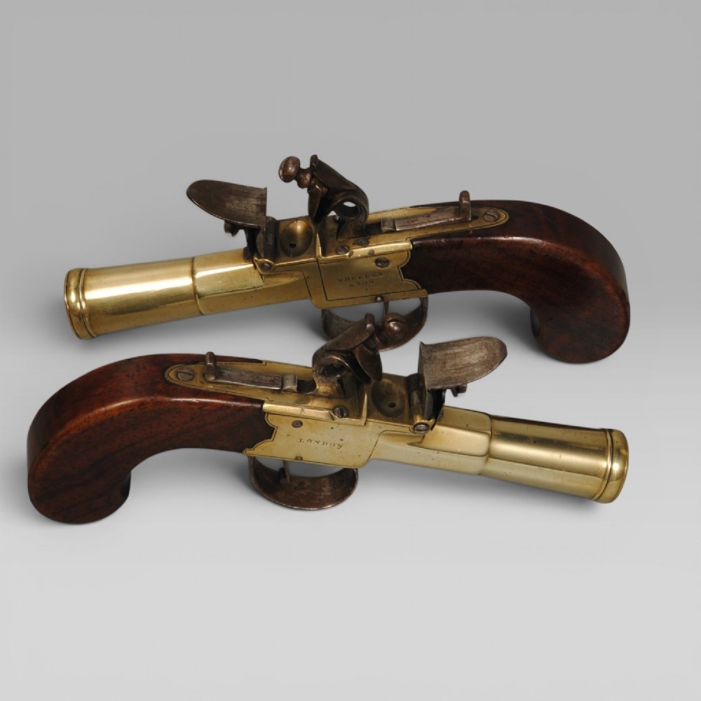 A pair of antique Georgian boxlock flintlock pistols featuring flared brass barrels, steel mechanisms, and dark wood grips.