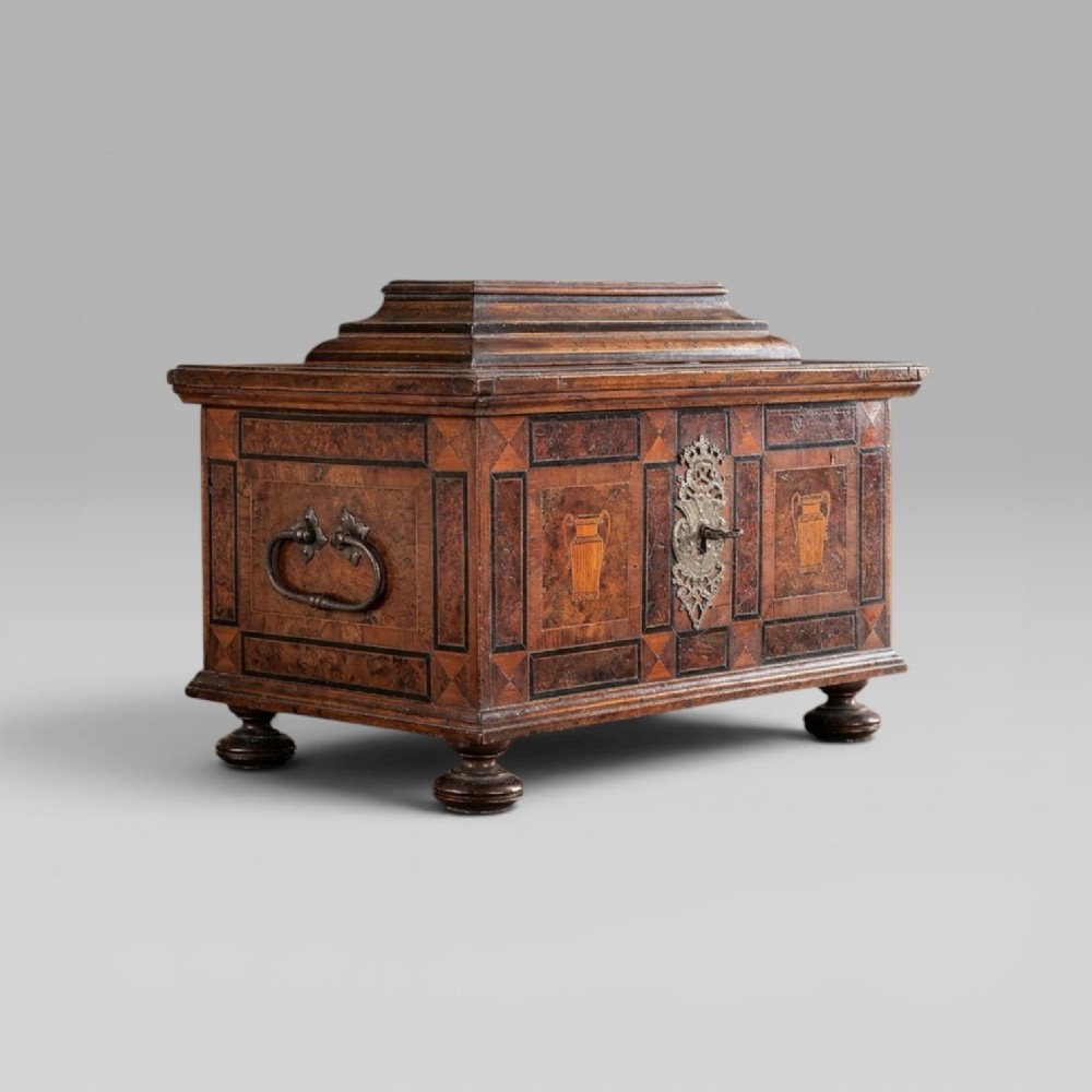 A late 17th-century Continental burr wood casket with a stepped lid, inlaid urn motifs, side iron handles, and a decorative keyhole escutcheon resting on bun feet.