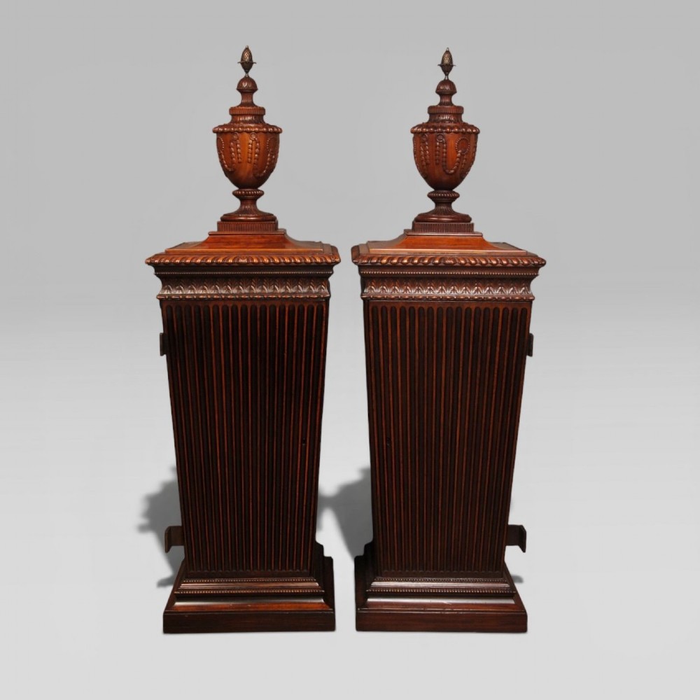A pair of 18th-century mahogany dining pedestals featuring fluted square bodies, moulded bases, and detailed carved urn finials.