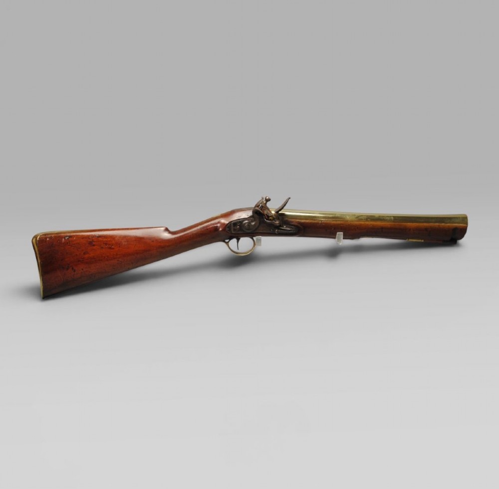 A Georgian flintlock blunderbuss featuring a flared brass barrel, steel lock plate, and polished walnut wooden stock.