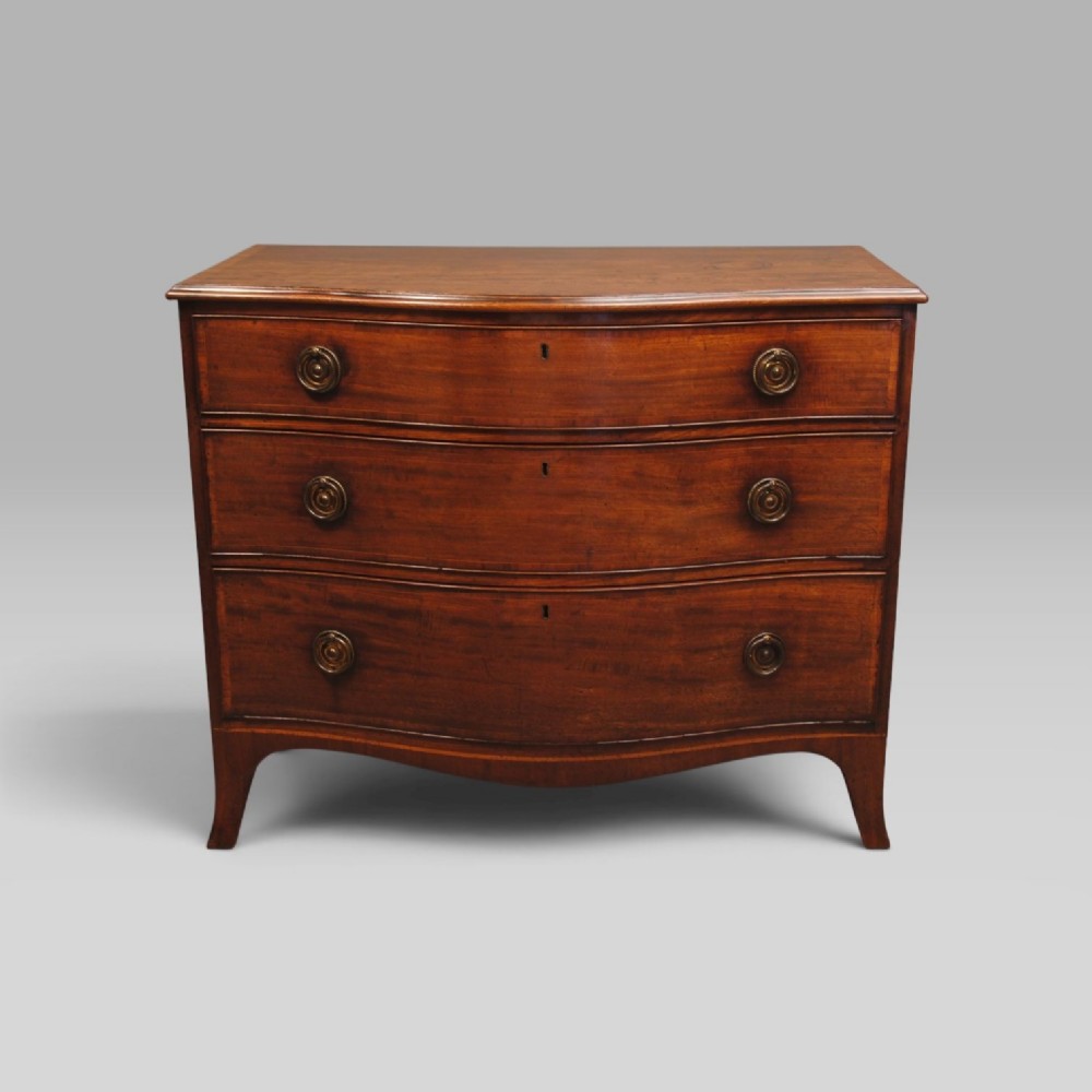 A mahogany chest of drawers featuring a serpentine curved front, three long drawers with circular brass drop handles, and splayed bracket feet.