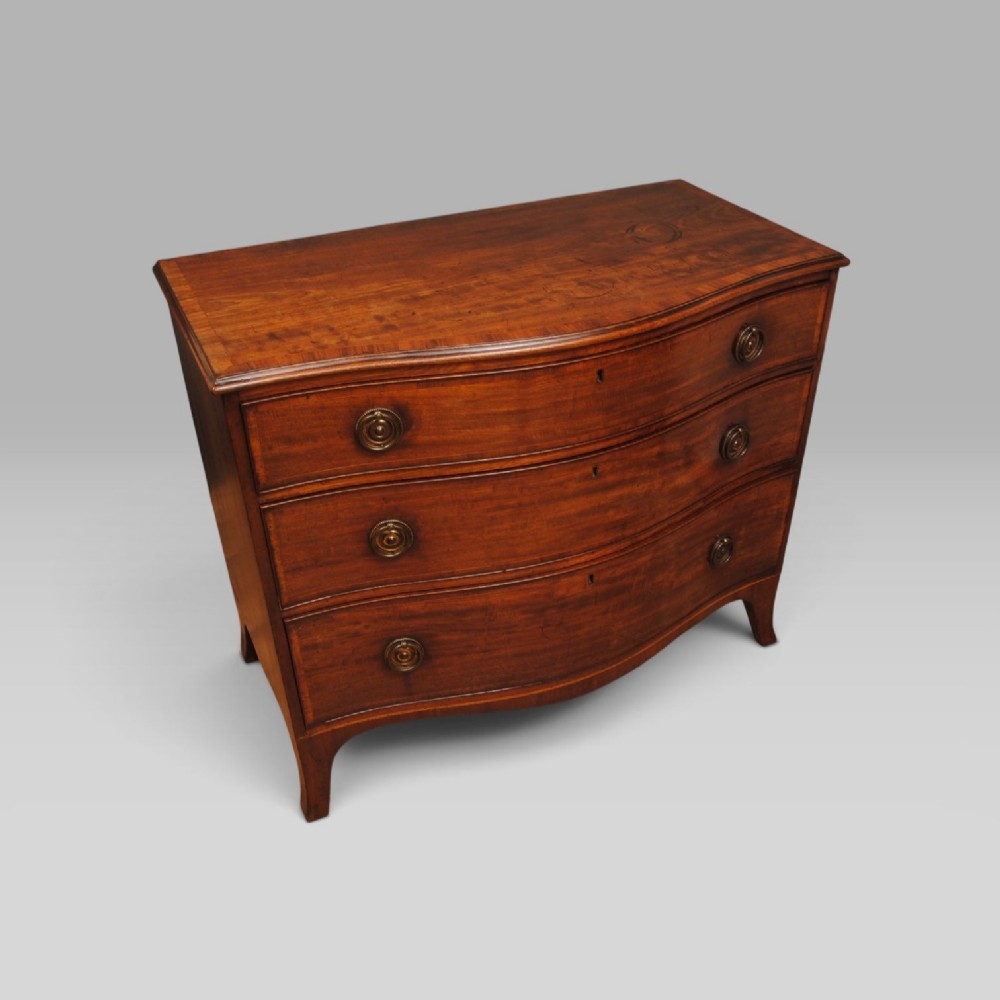 A mahogany chest of drawers featuring a serpentine curved front, three long drawers with circular brass drop handles, and splayed bracket feet. View II