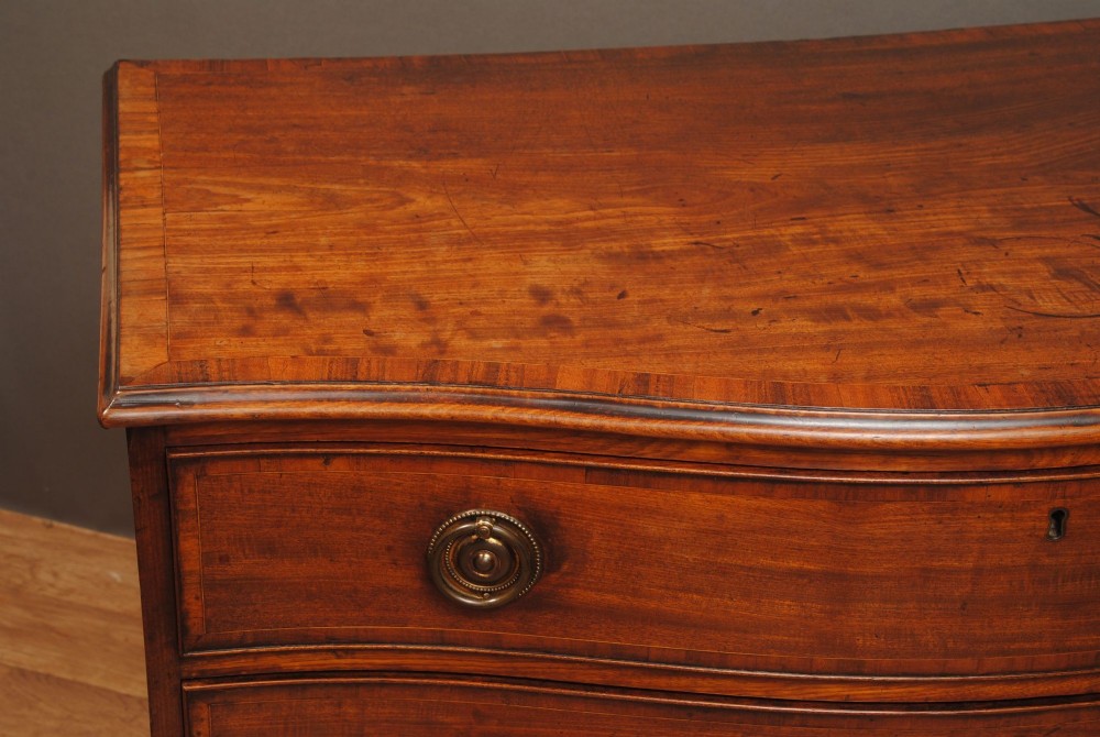 A mahogany chest of drawers featuring a serpentine curved front, three long drawers with circular brass drop handles, and splayed bracket feet. View III