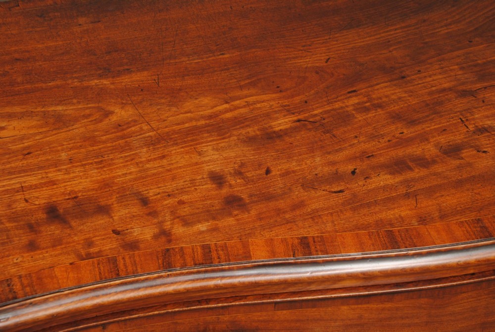 A mahogany chest of drawers featuring a serpentine curved front, three long drawers with circular brass drop handles, and splayed bracket feet. View IV