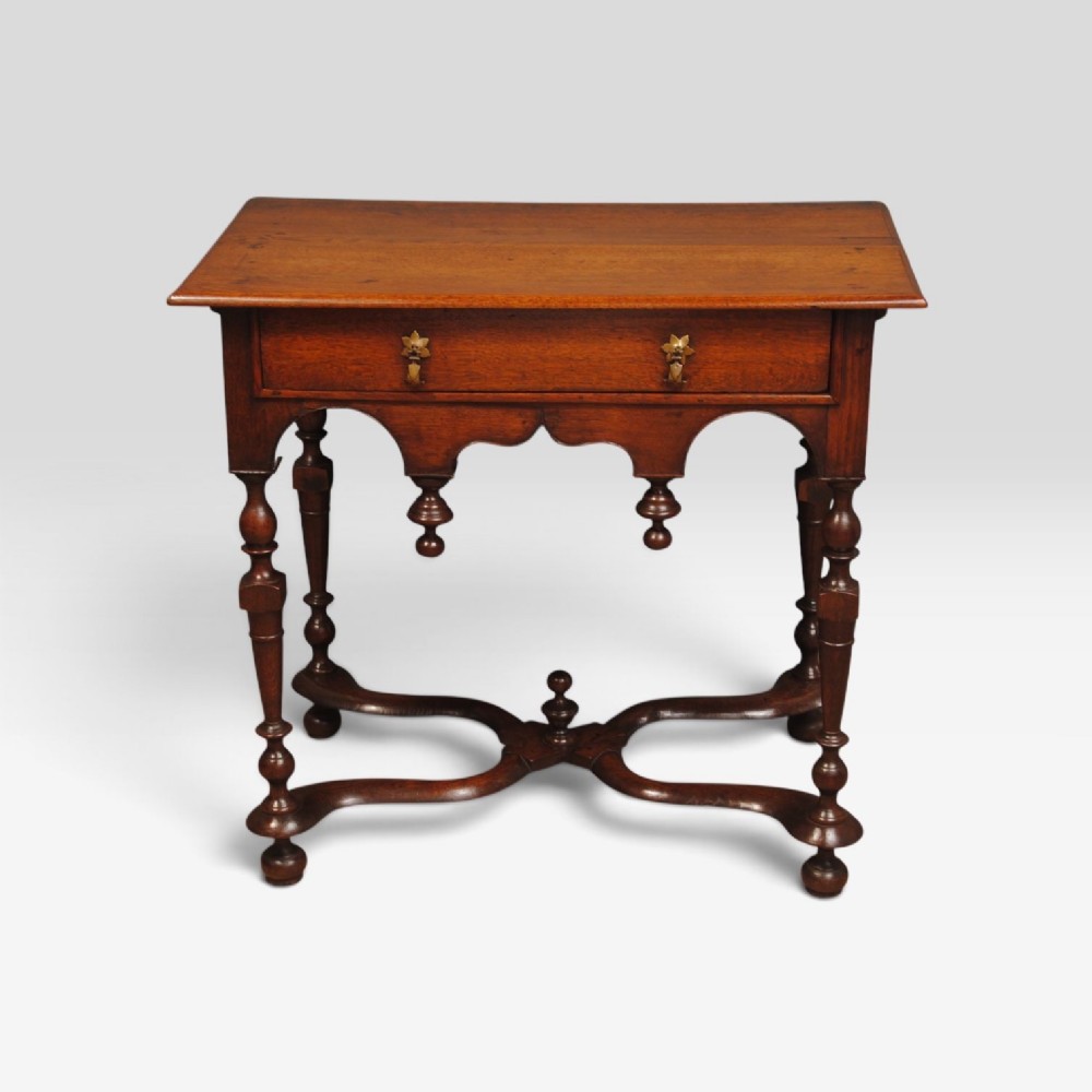 An eighteenth-century Queen Anne oak lowboy featuring turned legs, a single drawer with brass pulls, a shaped apron with drop finials, and a curved X-stretcher. View II