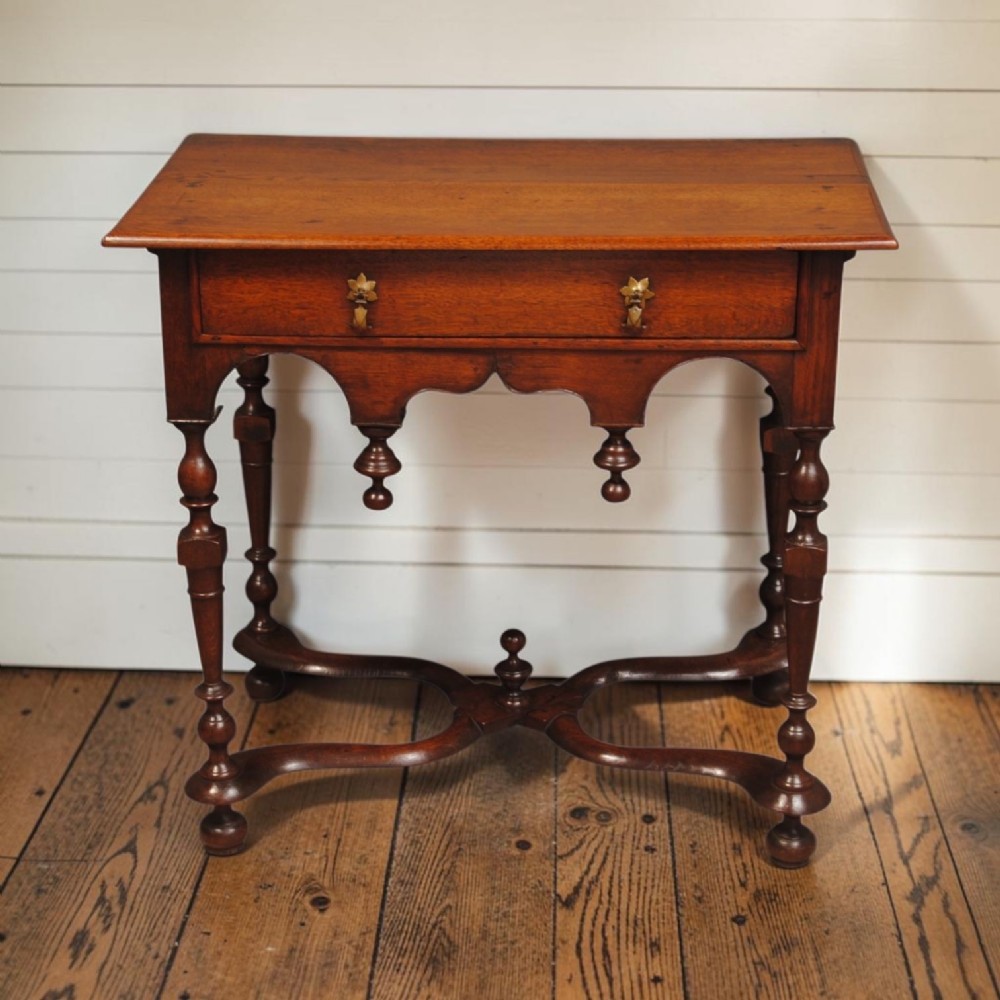 An eighteenth-century Queen Anne oak lowboy featuring turned legs, a single drawer with brass pulls, a shaped apron with drop finials, and a curved X-stretcher. View IV