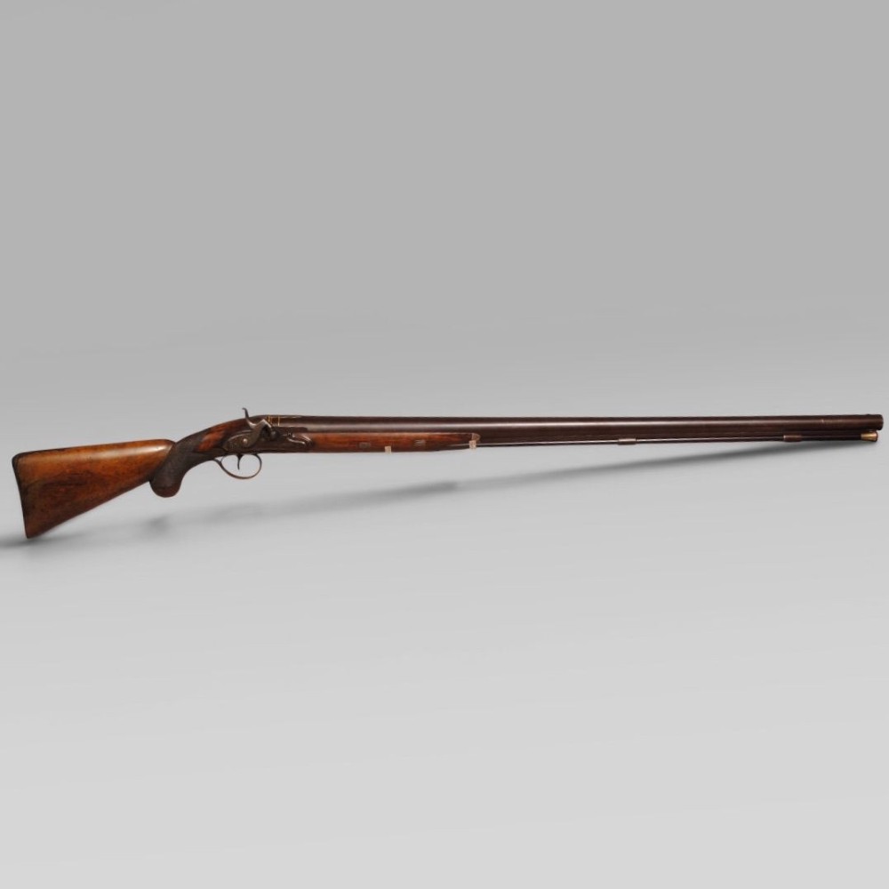 An antique six bore percussion fowling piece with an extended steel barrel and dark walnut stock.