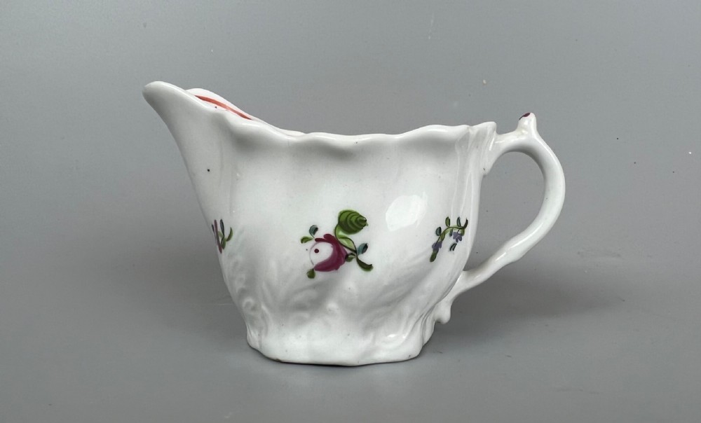 An 18th-century white soft-paste porcelain low Chelsea ewer decorated with hand-painted floral sprigs and leaf moulding.