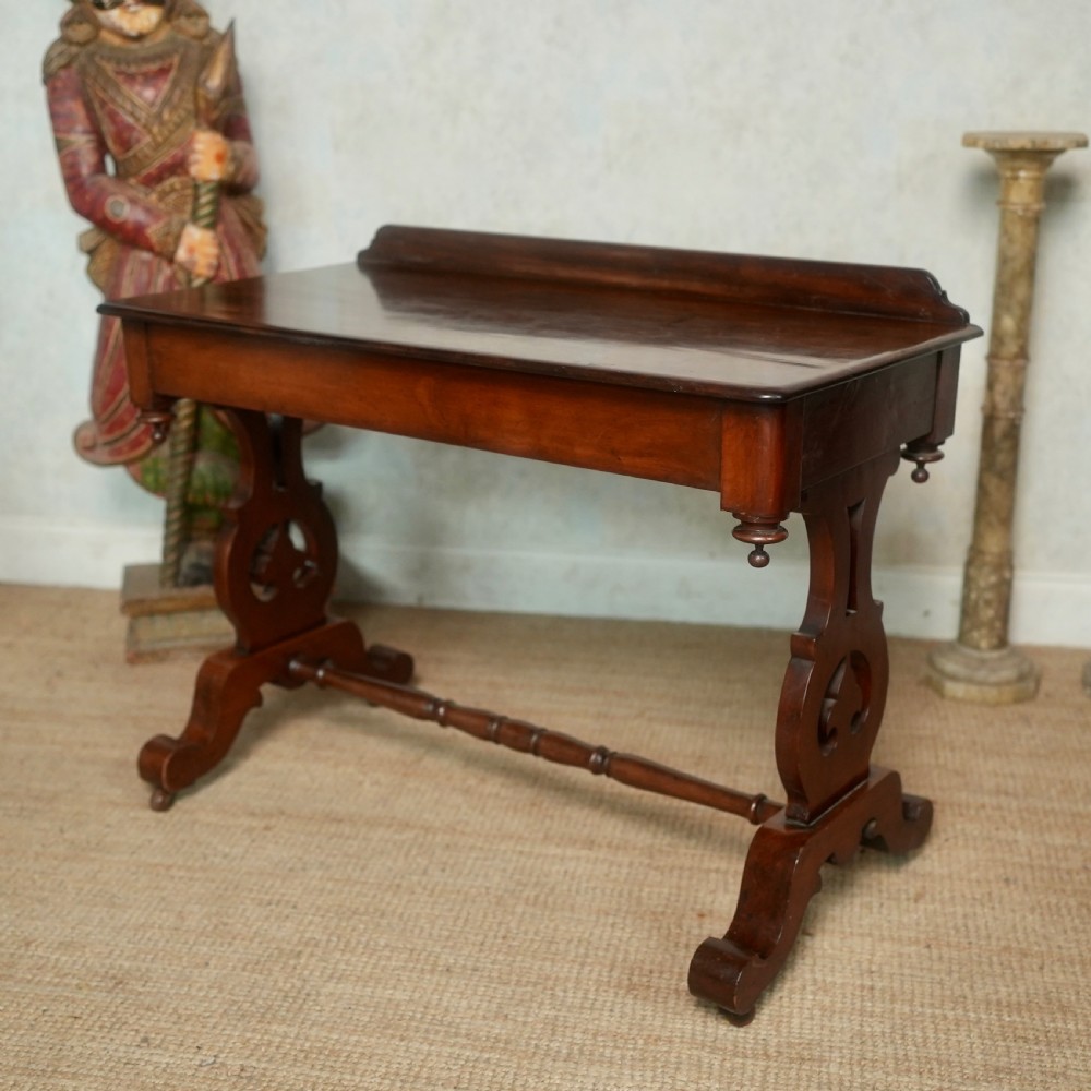 Victorian mahogany writing table with a low rear gallery, turned stretcher, and shaped trestle end supports on castors. View III