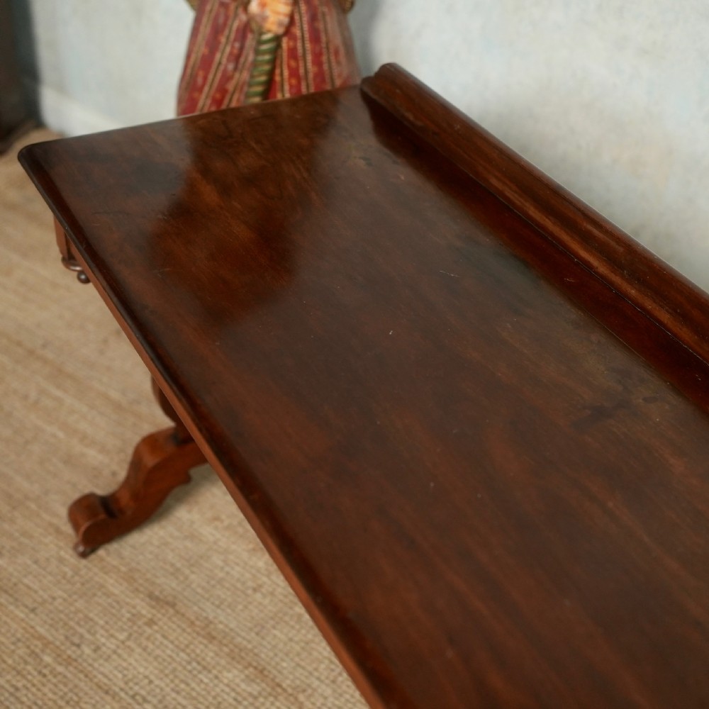 Victorian mahogany writing table with a low rear gallery, turned stretcher, and shaped trestle end supports on castors. View V