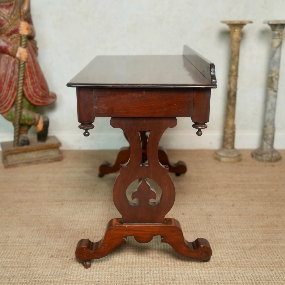 Victorian mahogany writing table with a low rear gallery, turned stretcher, and shaped trestle end supports on castors. View VI