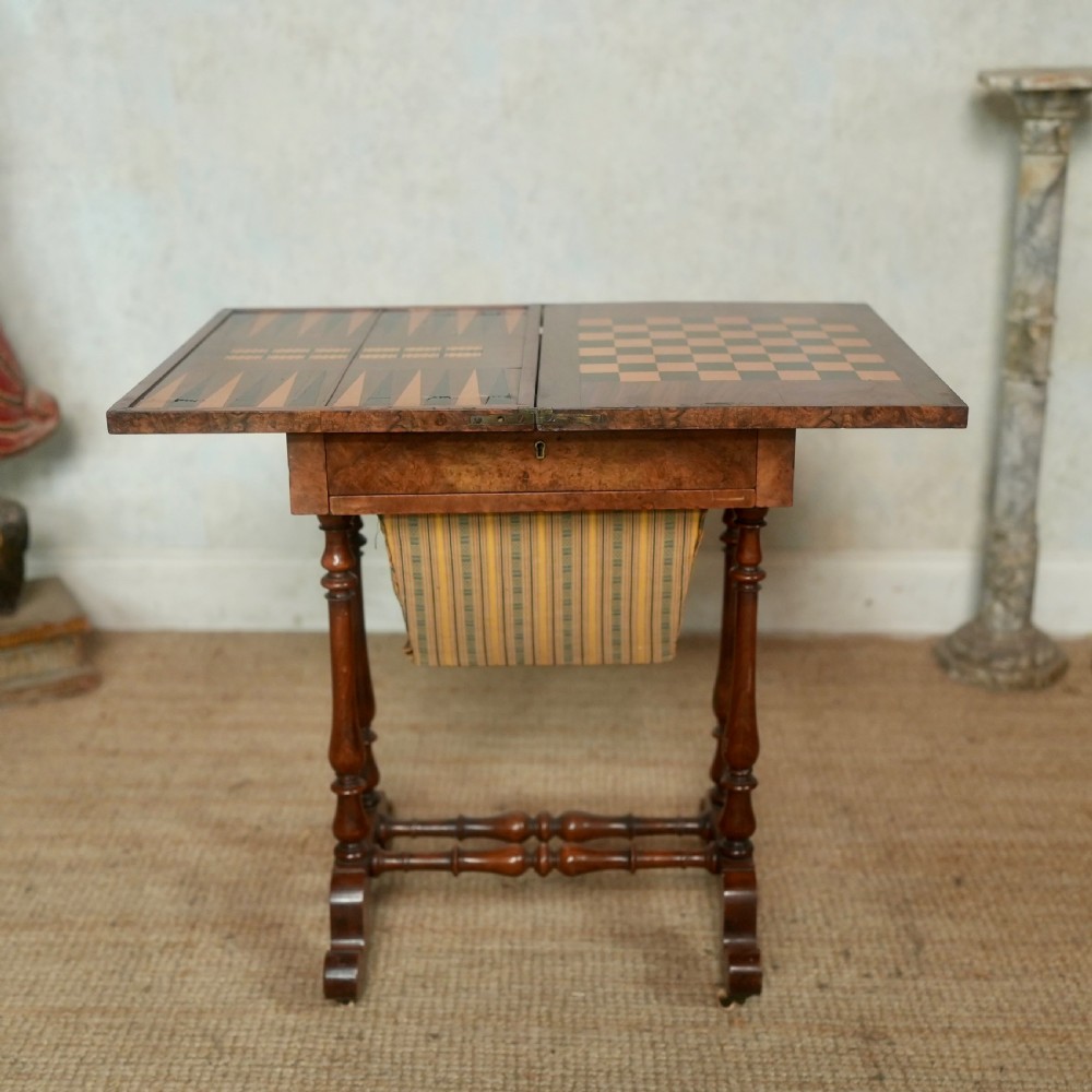 A nineteenth-century rosewood games table featuring a swivel folding top with inlaid chess and backgammon boards, resting on turned trestle supports with a fabric sewing basket underneath. View III