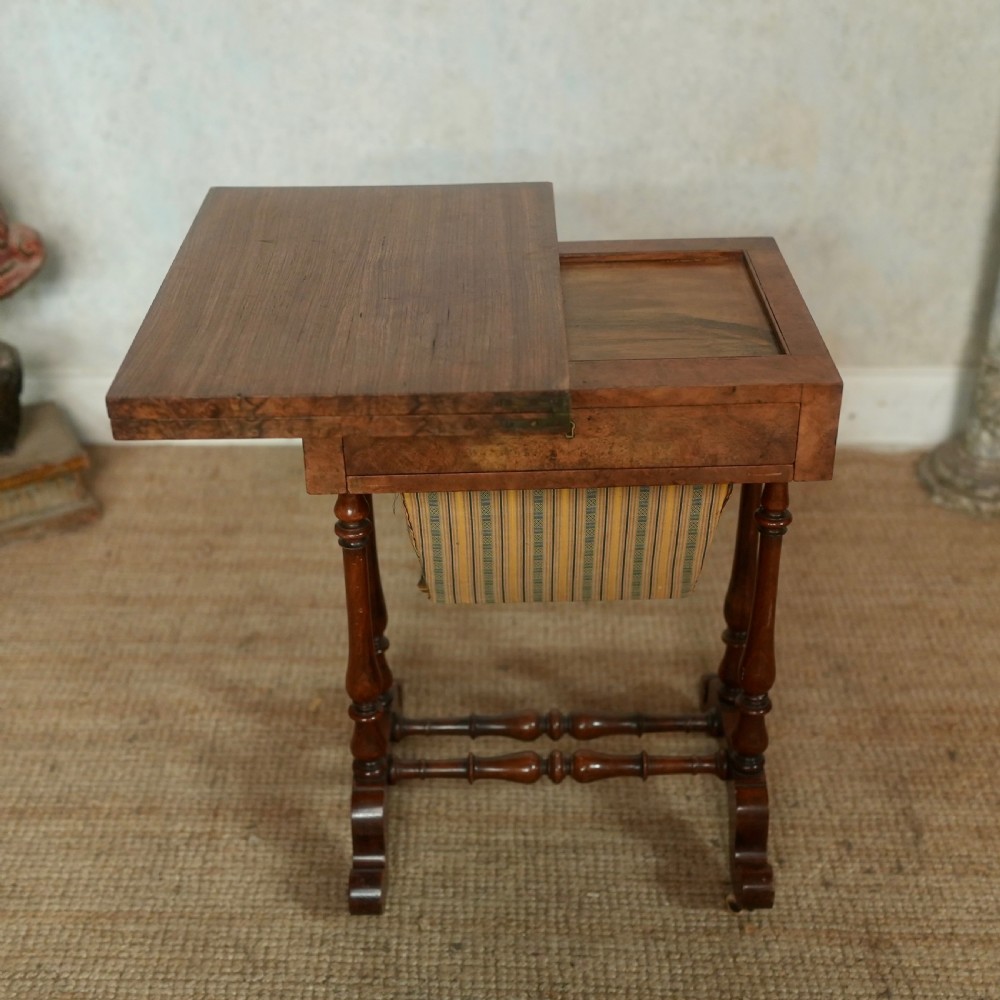 A nineteenth-century rosewood games table featuring a swivel folding top with inlaid chess and backgammon boards, resting on turned trestle supports with a fabric sewing basket underneath. View VI