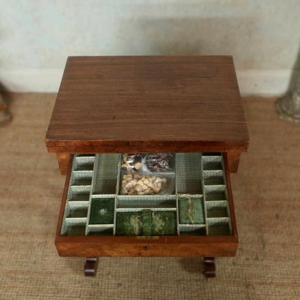 A nineteenth-century rosewood games table featuring a swivel folding top with inlaid chess and backgammon boards, resting on turned trestle supports with a fabric sewing basket underneath. View X