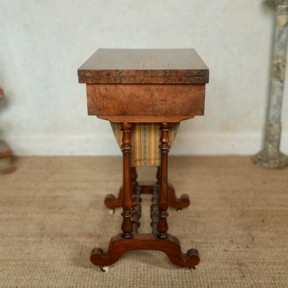 A nineteenth-century rosewood games table featuring a swivel folding top with inlaid chess and backgammon boards, resting on turned trestle supports with a fabric sewing basket underneath. View XIII