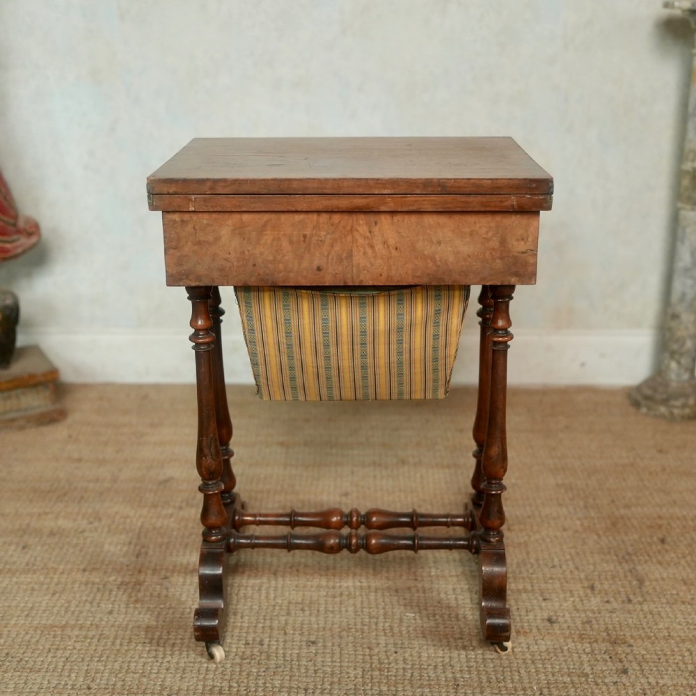 A nineteenth-century rosewood games table featuring a swivel folding top with inlaid chess and backgammon boards, resting on turned trestle supports with a fabric sewing basket underneath. View XIV