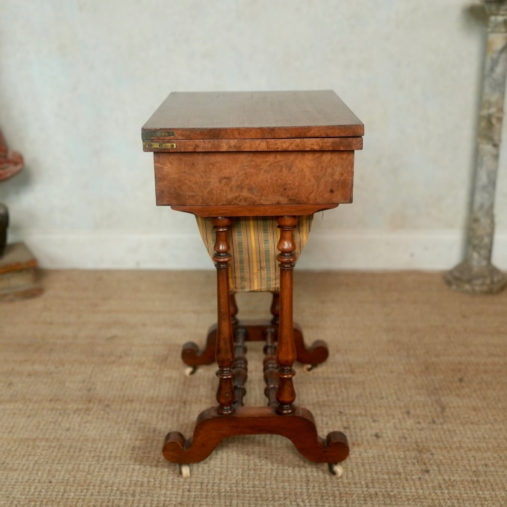A nineteenth-century rosewood games table featuring a swivel folding top with inlaid chess and backgammon boards, resting on turned trestle supports with a fabric sewing basket underneath. View XV