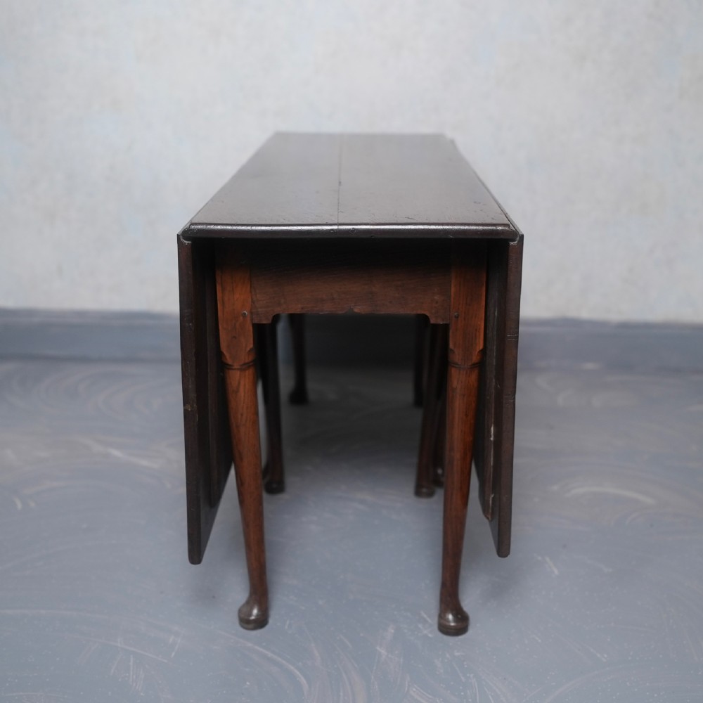 An 18th-century oak gateleg dining table featuring drop-leaf flaps supported by swinging legs terminating in pad feet. View XV