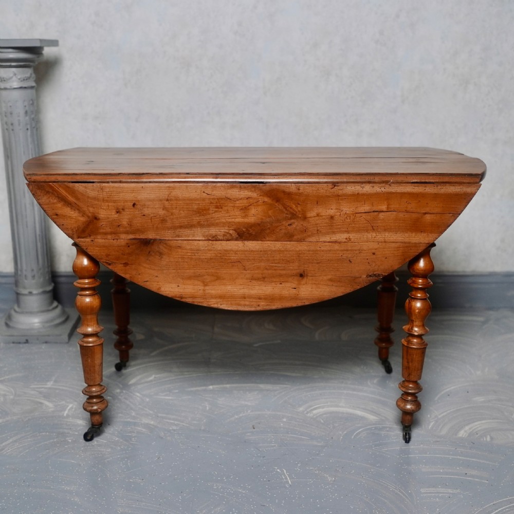 An antique French fruitwood drop-leaf dining table with turned legs, castors, and a warm honey-toned wood grain.