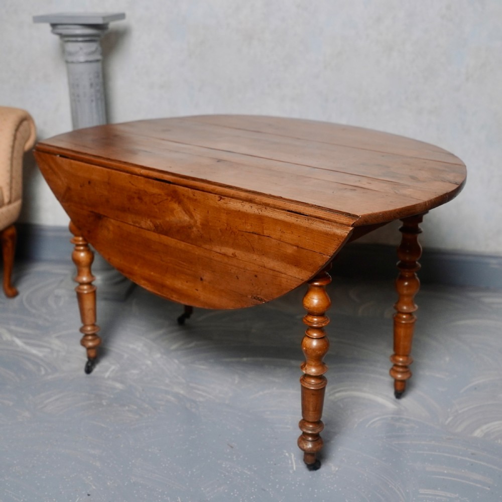 An antique French fruitwood drop-leaf dining table with turned legs, castors, and a warm honey-toned wood grain. View VI