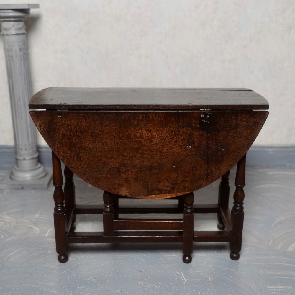 An eighteenth-century dark oak gateleg table shown with drop-leaf sides folded down, featuring turned legs and lower stretchers.