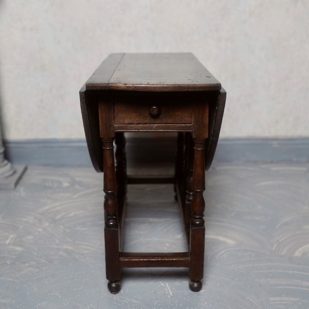 An eighteenth-century dark oak gateleg table shown with drop-leaf sides folded down, featuring turned legs and lower stretchers. View II