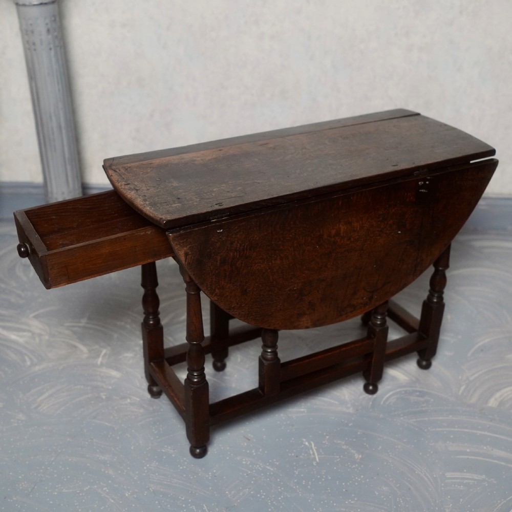 An eighteenth-century dark oak gateleg table shown with drop-leaf sides folded down, featuring turned legs and lower stretchers. View V