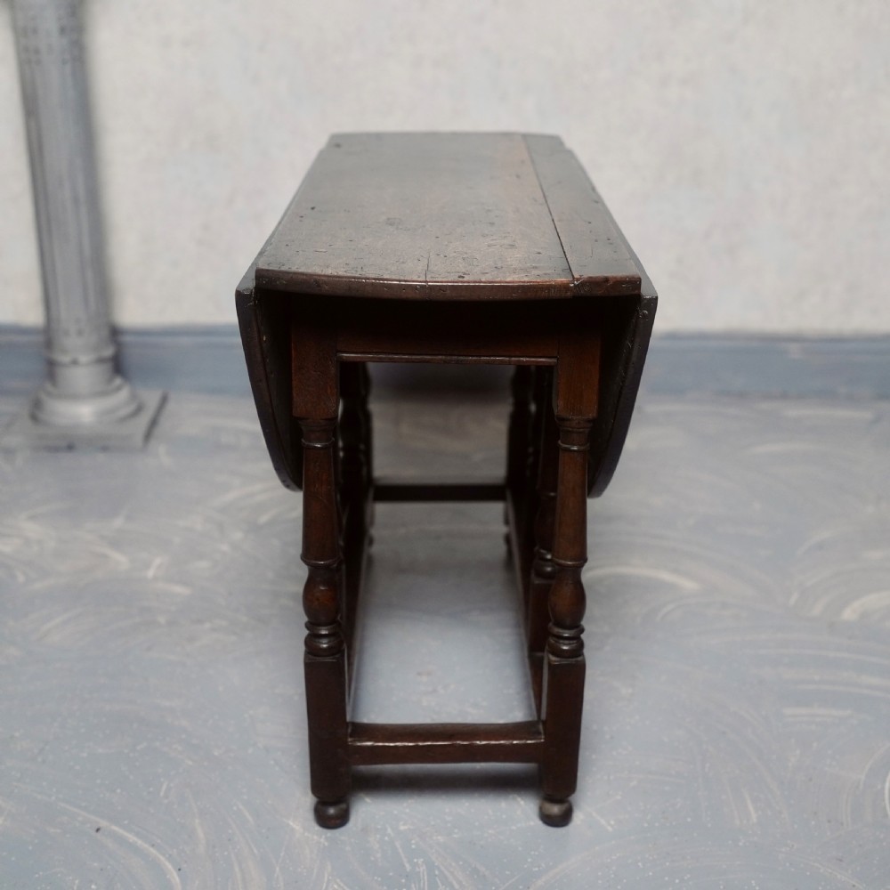 An eighteenth-century dark oak gateleg table shown with drop-leaf sides folded down, featuring turned legs and lower stretchers. View VI