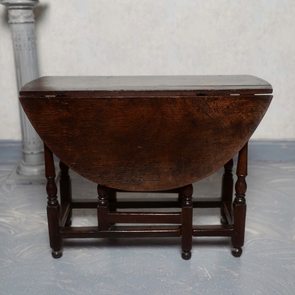 An eighteenth-century dark oak gateleg table shown with drop-leaf sides folded down, featuring turned legs and lower stretchers. View VII