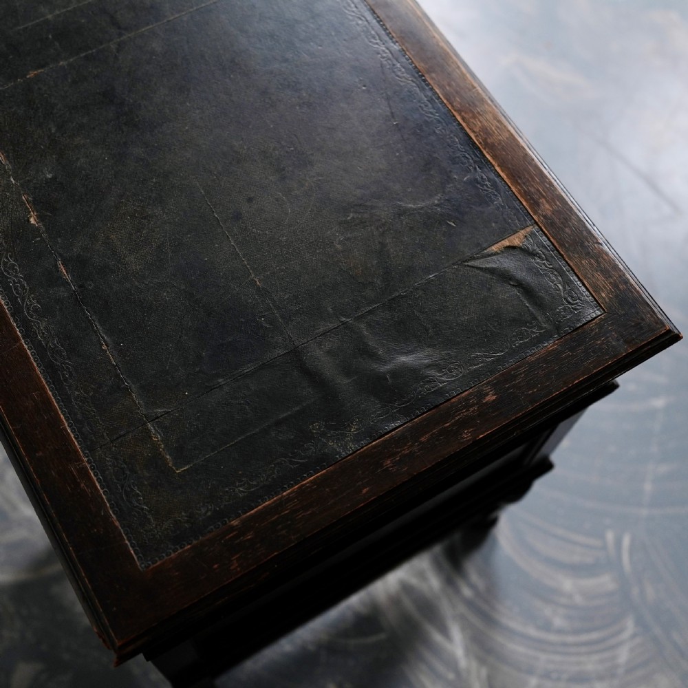 An antique dark oak kneehole desk featuring a leather-inset writing surface, six drawers with brass handles, and turned legs connected by stretchers. View III