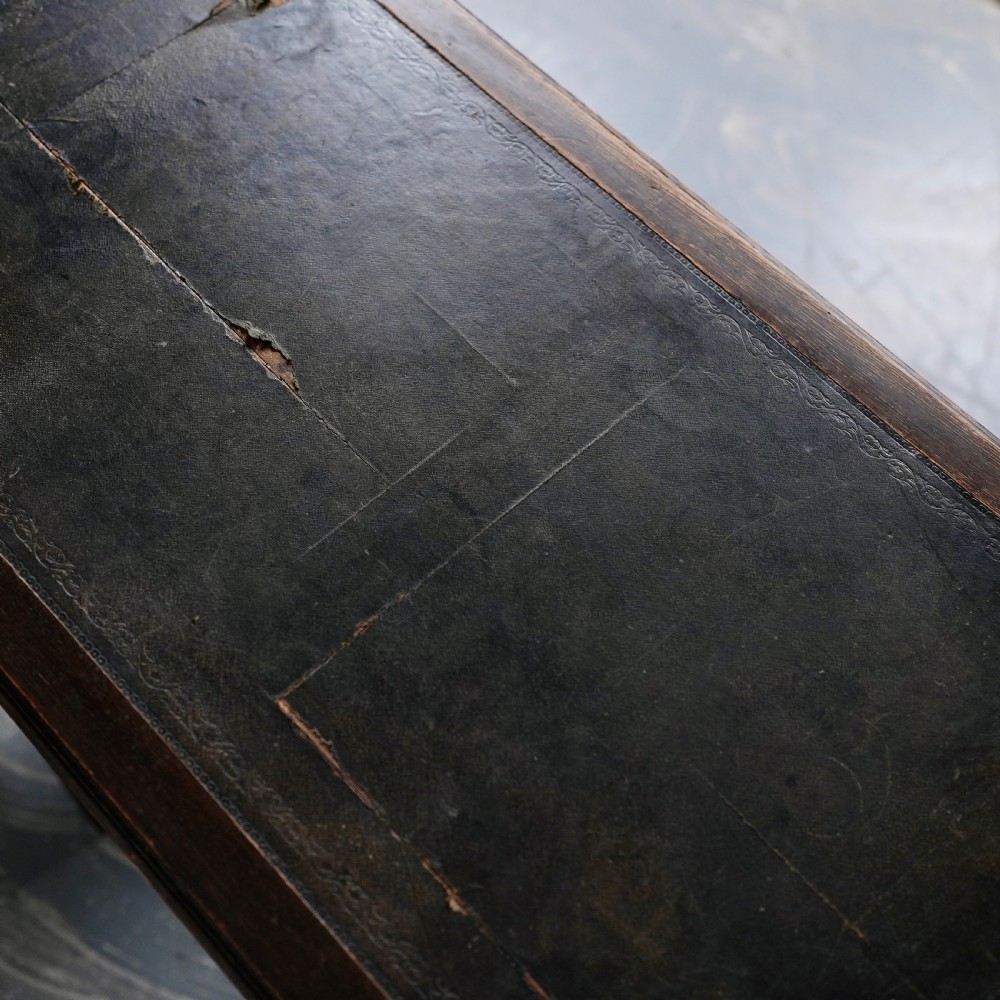 An antique dark oak kneehole desk featuring a leather-inset writing surface, six drawers with brass handles, and turned legs connected by stretchers. View V