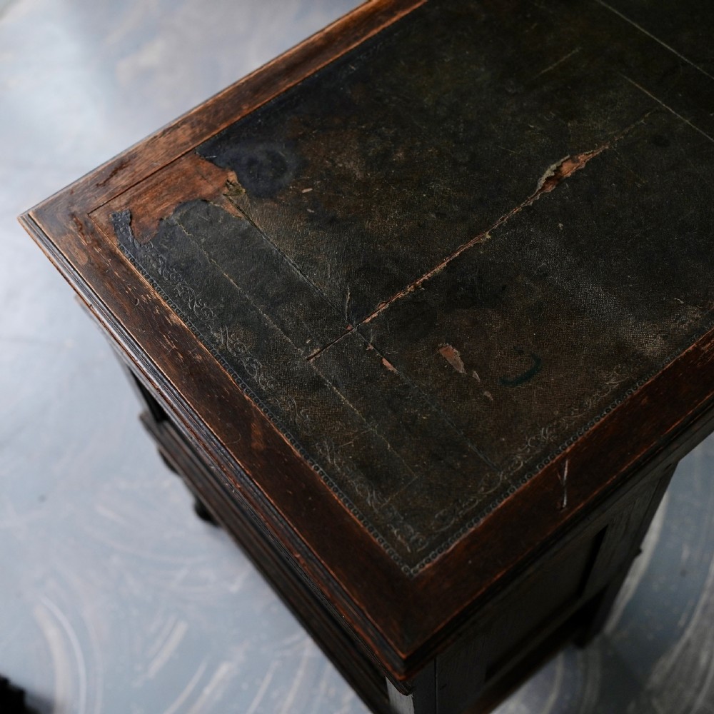 An antique dark oak kneehole desk featuring a leather-inset writing surface, six drawers with brass handles, and turned legs connected by stretchers. View VI