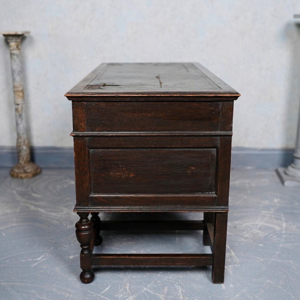 An antique dark oak kneehole desk featuring a leather-inset writing surface, six drawers with brass handles, and turned legs connected by stretchers. View XI