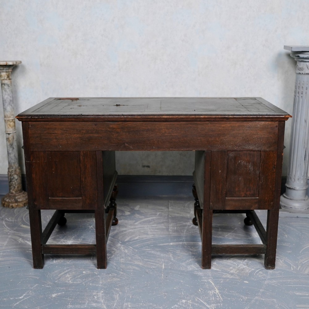 An antique dark oak kneehole desk featuring a leather-inset writing surface, six drawers with brass handles, and turned legs connected by stretchers. View XII