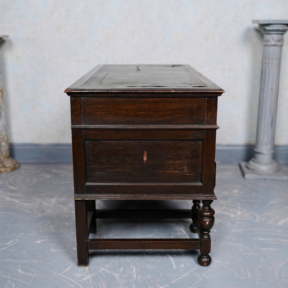 An antique dark oak kneehole desk featuring a leather-inset writing surface, six drawers with brass handles, and turned legs connected by stretchers. View XIII