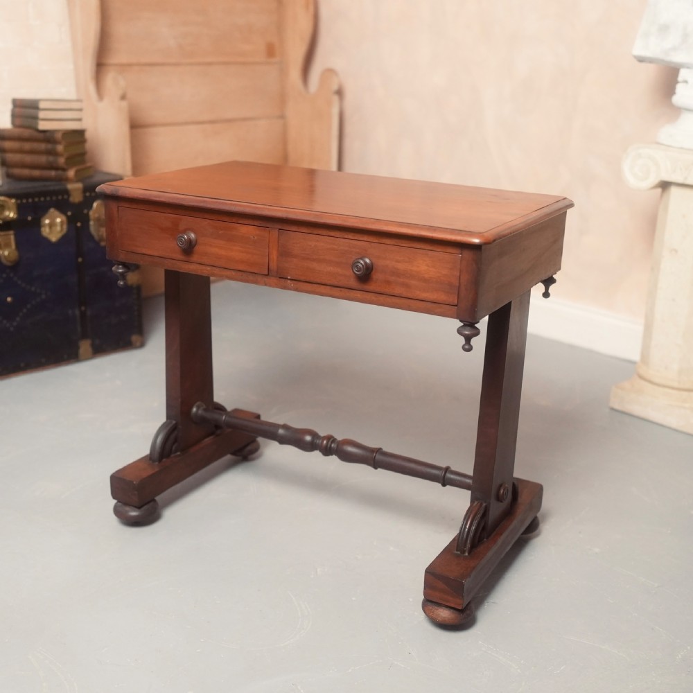A 19th-century mahogany writing table with two drawer fronts, turned wooden knobs, corner pendants, and a turned central stretcher between trestle legs.