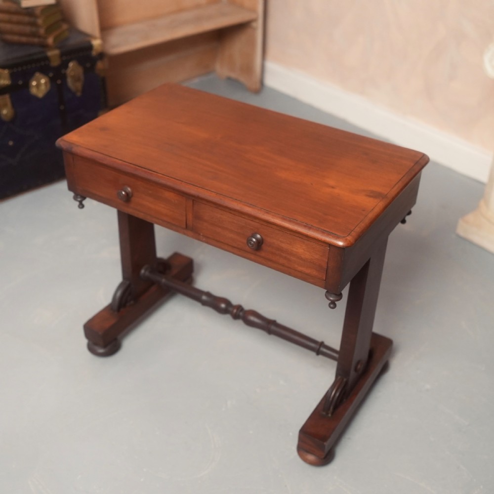 A 19th-century mahogany writing table with two drawer fronts, turned wooden knobs, corner pendants, and a turned central stretcher between trestle legs. View II
