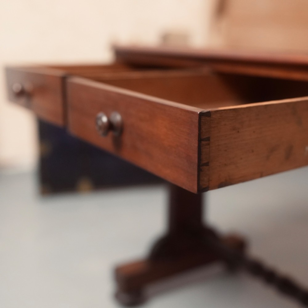A 19th-century mahogany writing table with two drawer fronts, turned wooden knobs, corner pendants, and a turned central stretcher between trestle legs. View IV