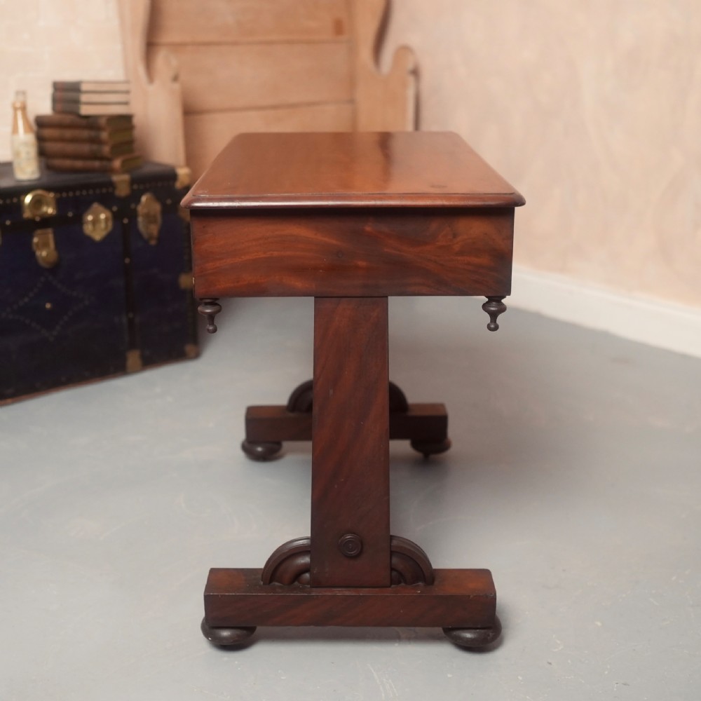 A 19th-century mahogany writing table with two drawer fronts, turned wooden knobs, corner pendants, and a turned central stretcher between trestle legs. View IX