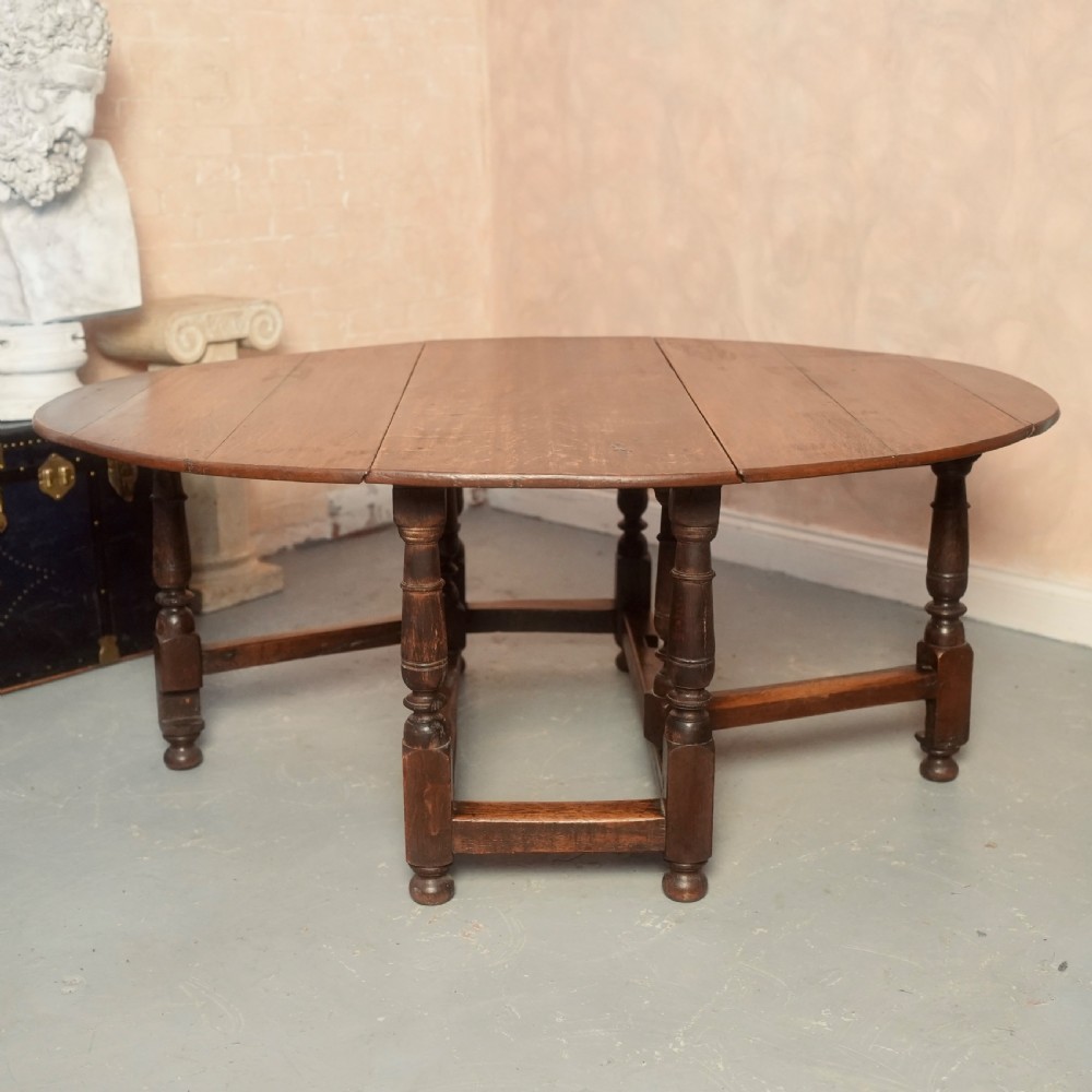 An 18th-century Georgian oak gateleg dining table featuring a round drop-leaf top, turned legs, and stretchers in a dark brown finish.