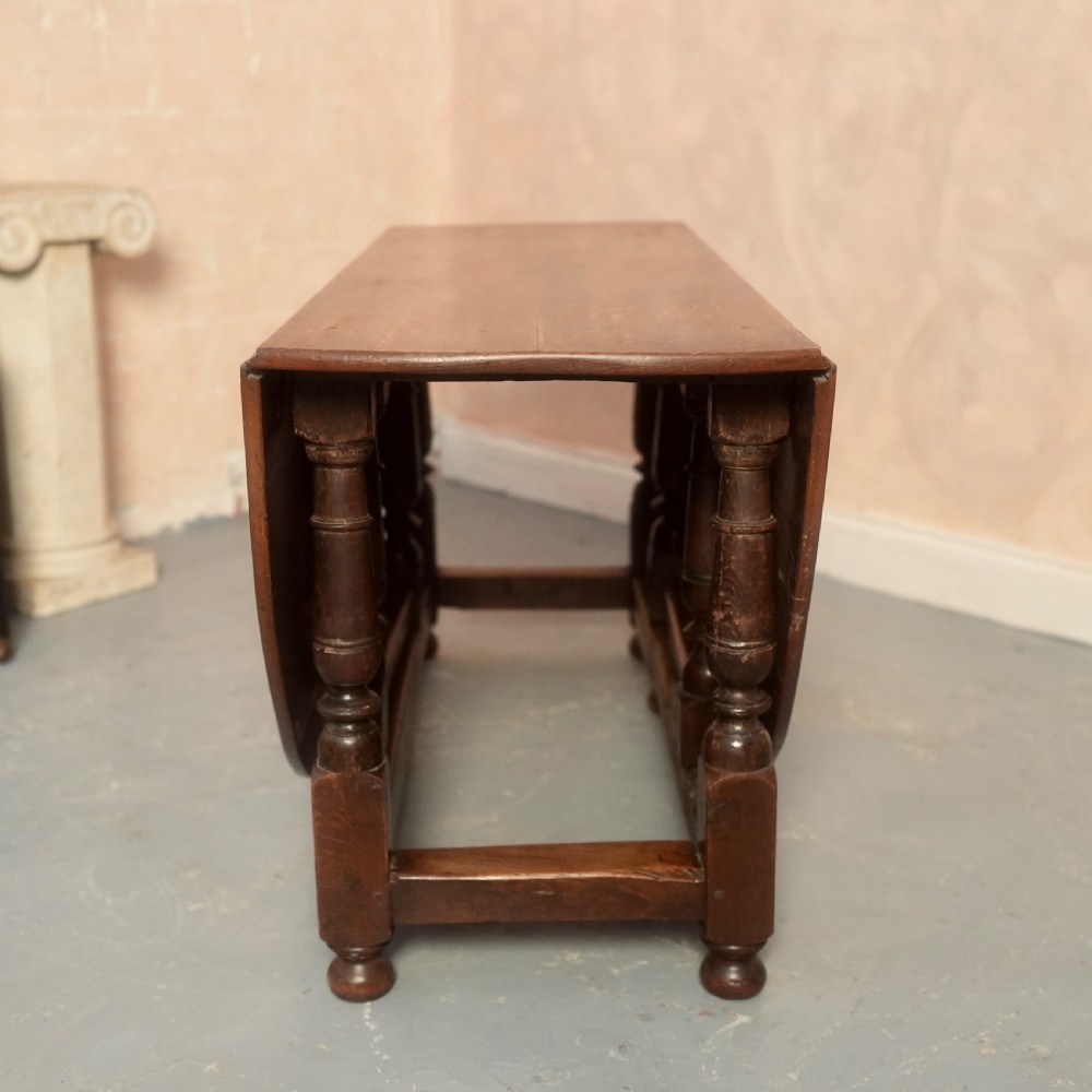 An 18th-century Georgian oak gateleg dining table featuring a round drop-leaf top, turned legs, and stretchers in a dark brown finish. View II