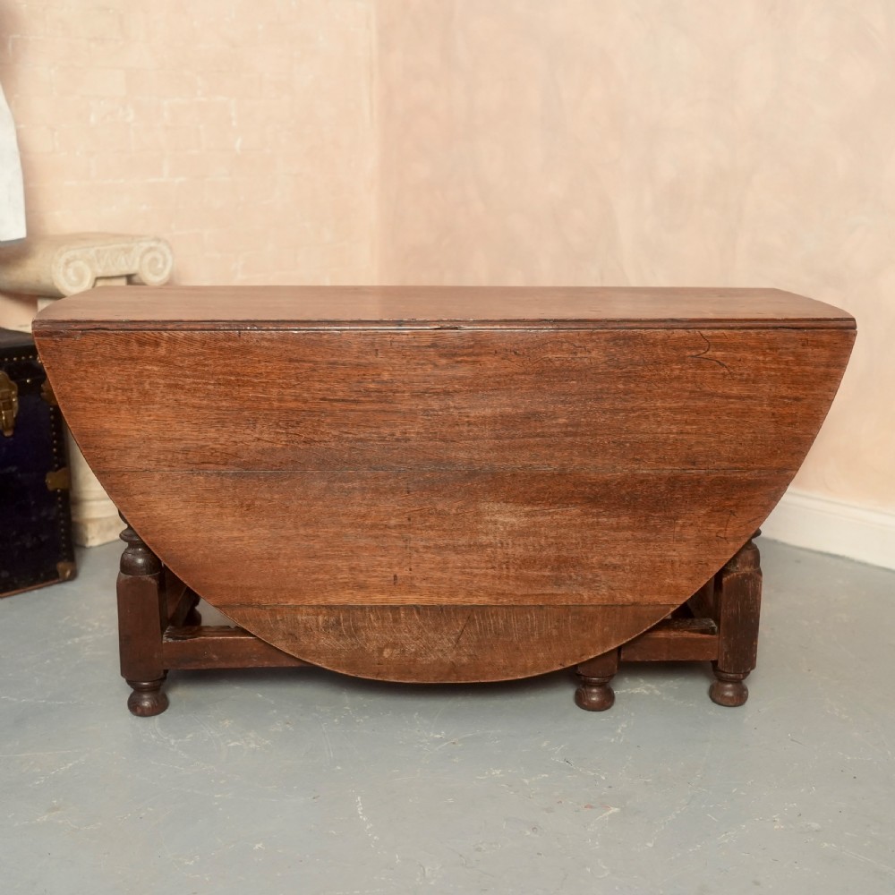 An 18th-century Georgian oak gateleg dining table featuring a round drop-leaf top, turned legs, and stretchers in a dark brown finish. View III