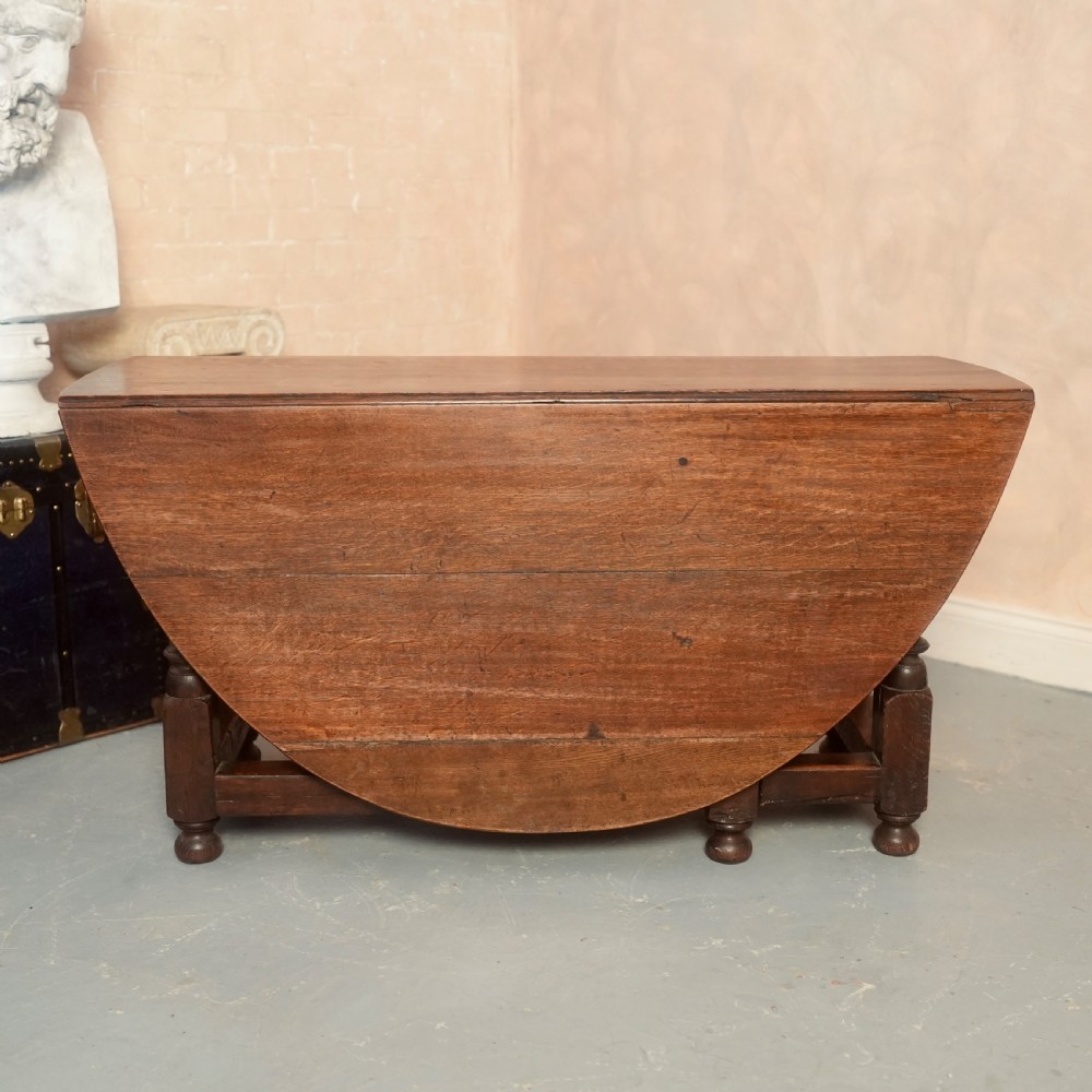 An 18th-century Georgian oak gateleg dining table featuring a round drop-leaf top, turned legs, and stretchers in a dark brown finish. View IV