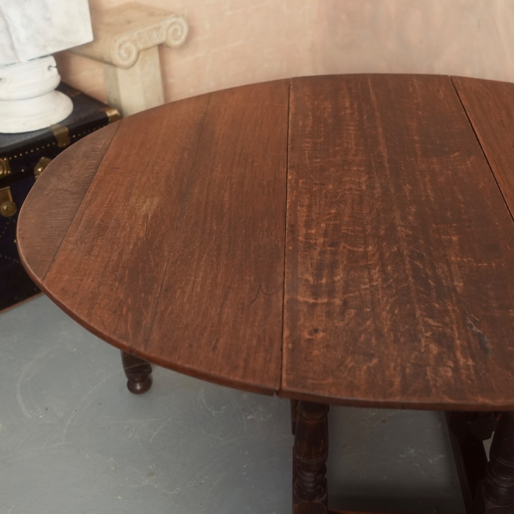An 18th-century Georgian oak gateleg dining table featuring a round drop-leaf top, turned legs, and stretchers in a dark brown finish. View V