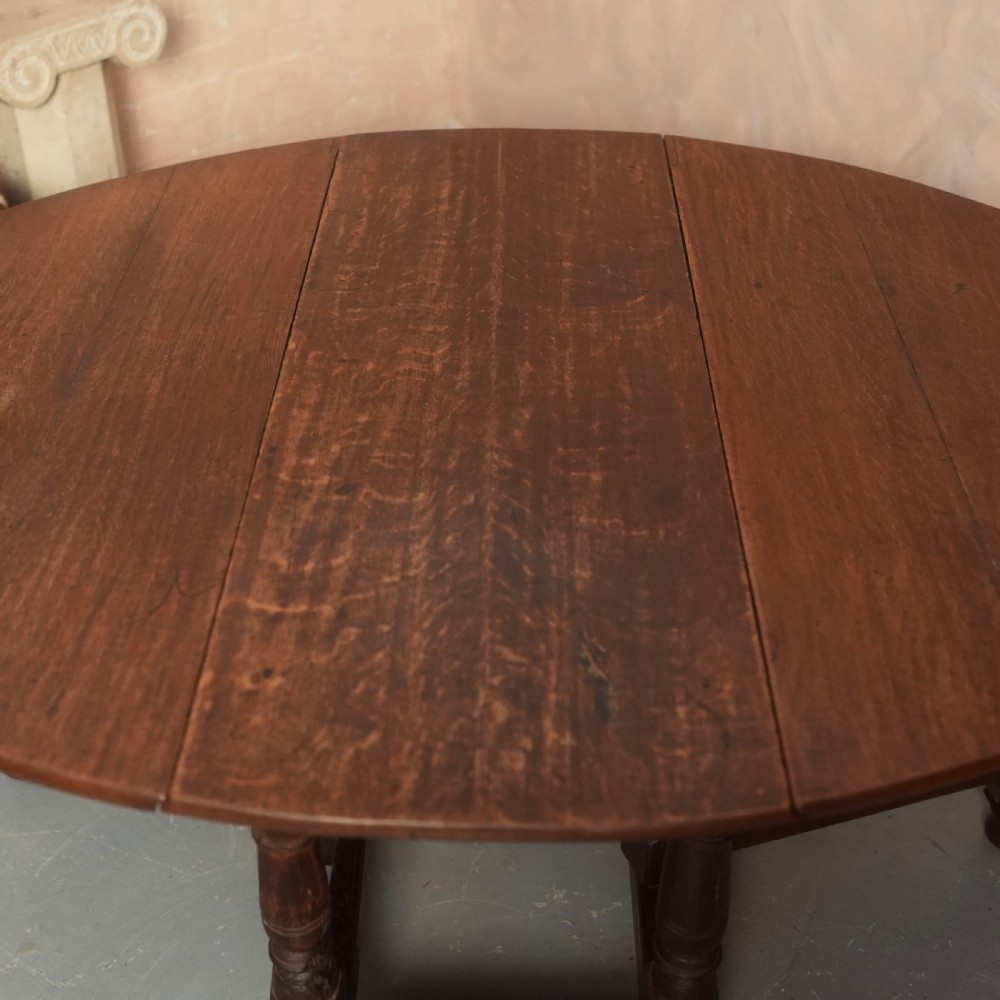 An 18th-century Georgian oak gateleg dining table featuring a round drop-leaf top, turned legs, and stretchers in a dark brown finish. View VI